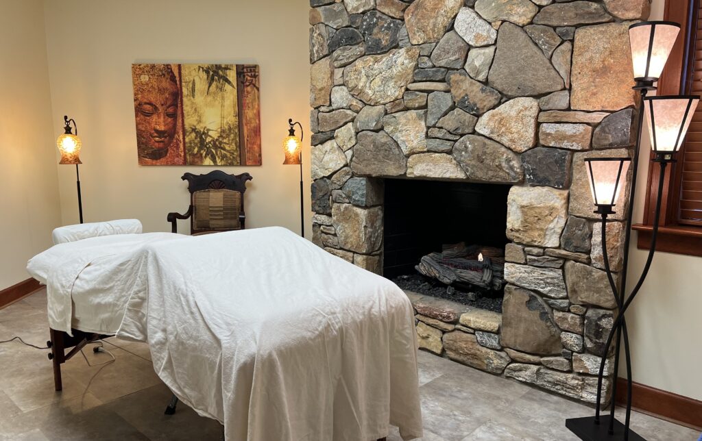 massage table in tranquil room with Buddhist-inspired art, gentle lighting, and stone hearth lit with crackling fire