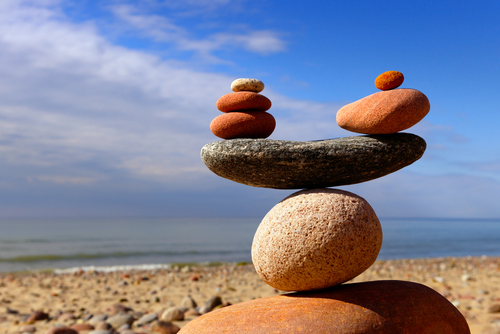 Rocks on a seashore in front of the waves on a beautiful sunny day.  The rocks have been placed atop one another to show different size rocks on each side of a larger, flat rock, to maintain the balance of the whole structure, which is balanced on a round rock.