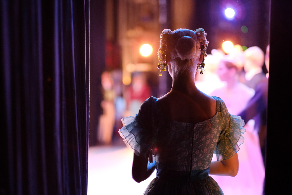 Young dancer backstage, peering through curtain as she awaits her cue to go onstage