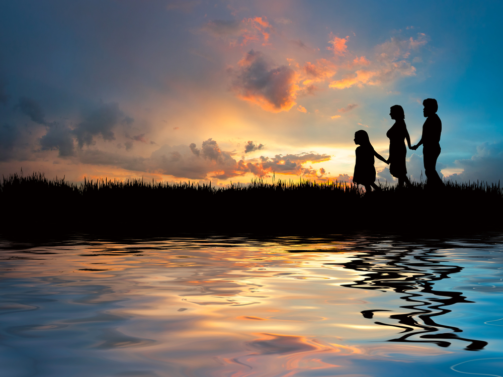 What appears to be a mother and father with a young girl walking hand in hand at sunset through rushes by a still body of water.  The little girl is in the lead.  The setting is peaceful and serene.